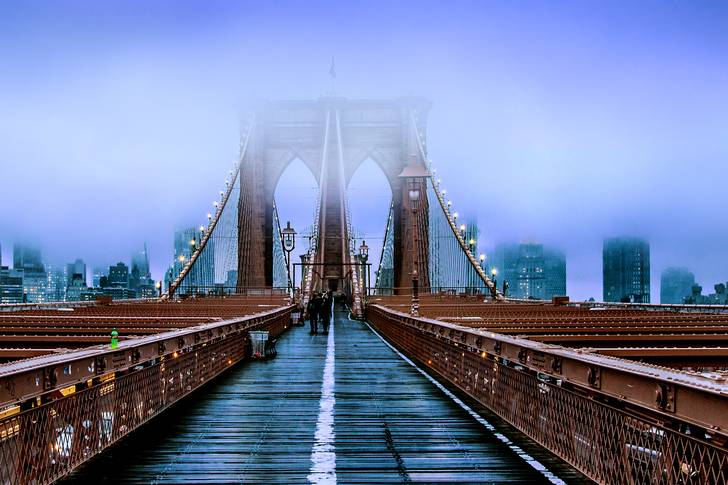 The Brooklyn Bridge is covered in fog.
